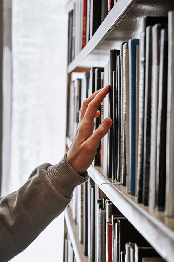 A person's hand reaches toward books on a library shelf.