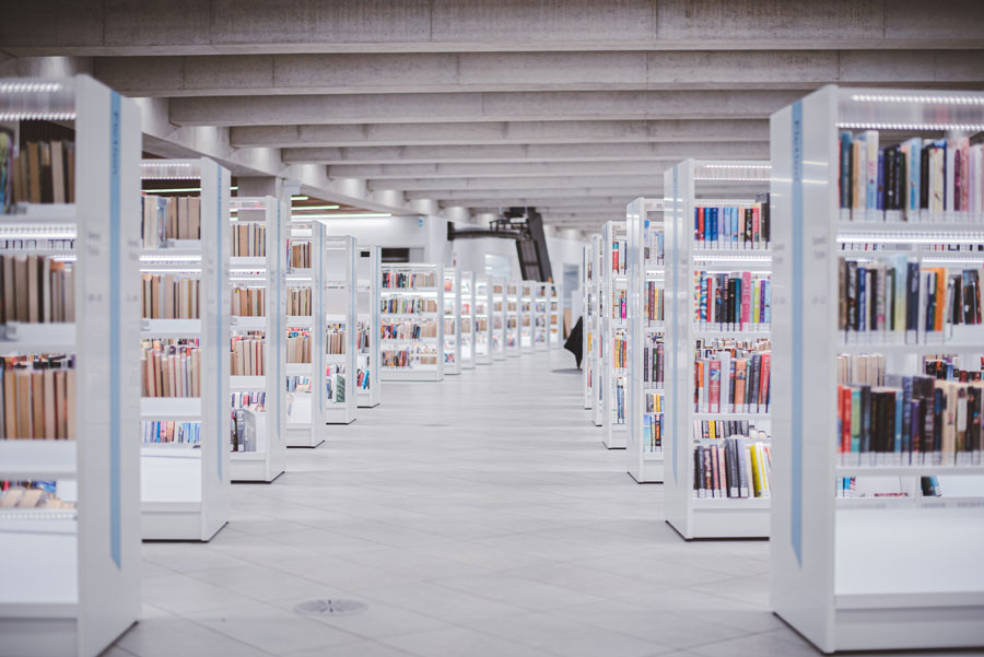 Wide view of a modern library interior with rows of white bookshelves filled with books under a concrete ceiling.