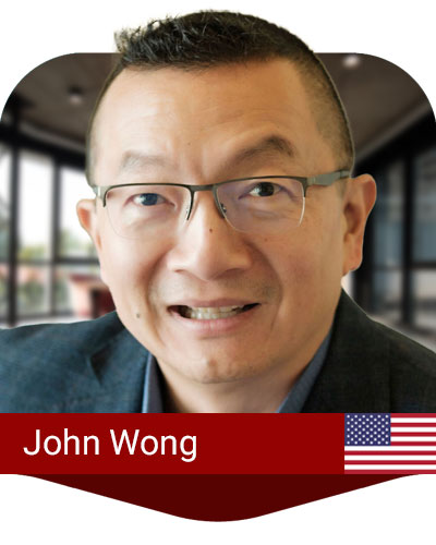 A man with short hair and glasses smiles indoors. A label at the bottom reads "John Wong" next to a small United States flag.