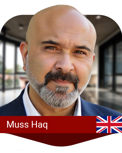 A bald man with a gray beard and mustache is shown in a suit jacket, standing in a modern indoor setting. A UK flag and the name "Muss Haq" appear at the bottom.